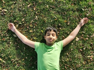 Child boy lie down on grasses or lawn under warm sunlight. Kid  closed his eyes and flew...