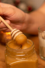 honey dripping from a jar in a christmas new year interior on a wooden table with candles around, winter holiday desserts