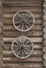 Obraz premium Two old wooden wheels fixed vertically on a log wall