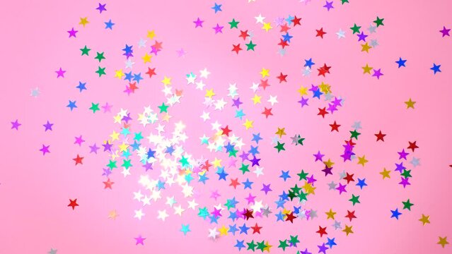Multicolored stars of confetti on pink background, top view