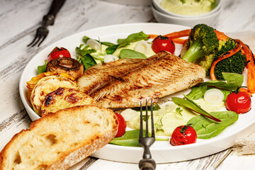 Sea fish and vegetables. Tilapia fillet with broccoli, cherry tomatoes and lettuce. Sea food on a white plate. Mediterranean diet concept - obrazy, fototapety, plakaty