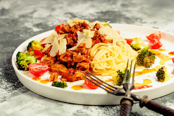 Close-up Appetizing pasta with meat in tomato sauce, vegetables and Parmesan cheese in a large white plate. Traditional mediterranean dish. Spaghetti with meat, broccoli, green peas and spices