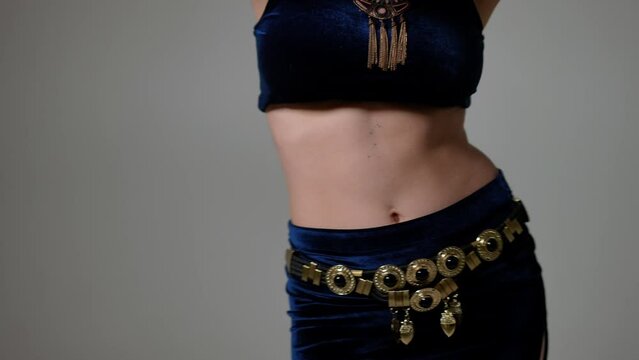 Back view slim belly dancer turning in slow motion shaking hips at grey background. Young Caucasian woman dancing belly dance moving gorgeous body
