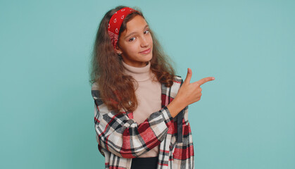 Happy preteen 12 years old girl showing thumb up pointing empty place, advertising area for commercial text, copy space for goods promotion. Young teen child kid. Studio shot on blue wall background