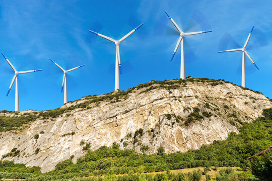 Group of white and blue wind turbines on the top of a mountain landscape, blue sky with clouds on background.