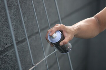 Closeup of man painting a fence with spray paint or aerosol paint