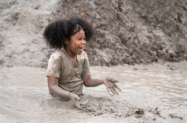 Funny African American kids girl playing in mud puddle	