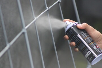 Closeup of man painting a fence with spray paint or aerosol paint - obrazy, fototapety, plakaty