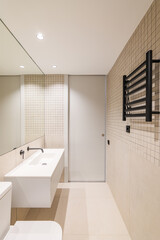 Vertical view of interior of modern bathroom with beige tiles, black radiator and white sink