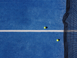 Overhead aerial view of two balls near the net of a blue paddle tennis court. Racket sports © VicVaz