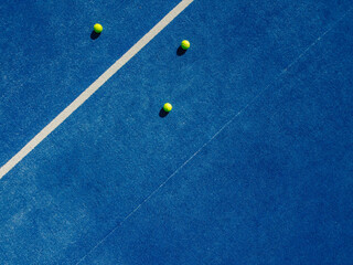 Overhead aerial view of three balls near the net of a blue paddle tennis court