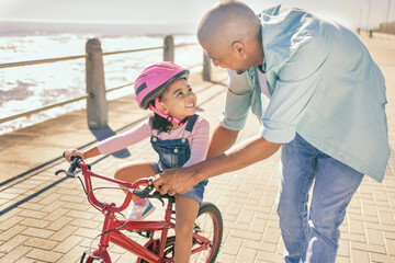 Father teaching his child to ride a bike at the beach while on a summer vacation, holiday or...
