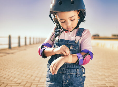 Cycling injury, arm bandage and child in street with bruise after fall or accident. First aid, bandaid and hurt city girl with safety helmet after playing, sports or fitness exercise alone on road.