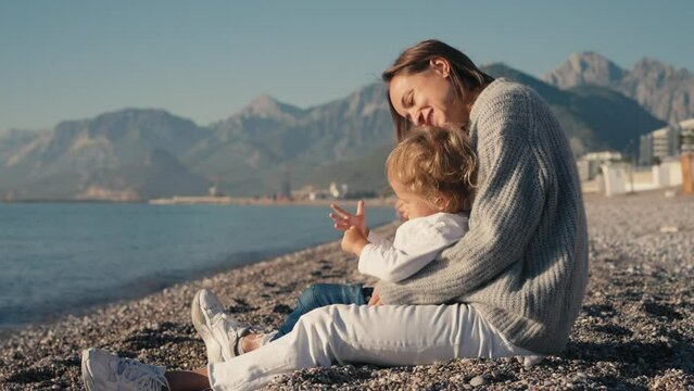 Mother playing with baby at the seahorse, beautiful sunrise, , woman embracing little child, parent love, sun shining over sea. High quality 4k footage