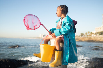 Girl, beach and fishing net with bucket, water and rock pool for outdoor adventure with boots,...