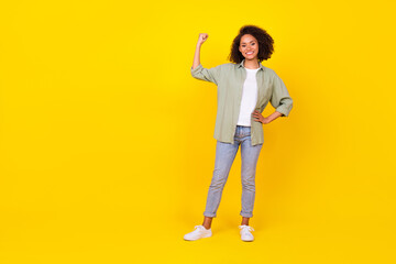 Full body photo of nice young girl wavy hair demonstrate power raise fist dressed stylish khaki clothes isolated on yellow color background