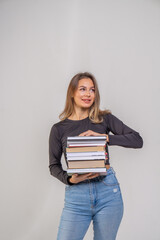 Attractive brown-haired girl in a black top and blue jeans holds a stack of books. Student with books preparing for the exam