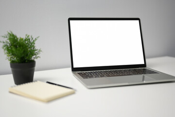 Mockup laptop computer with blank screen and notebook on white desk in office