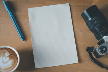 Top view of empty paper, coffee cup, camera and pen on the wooden table