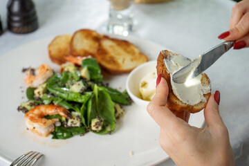female hands spread butter on bruschetta on the background of salad in a plate on the table
