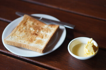 Closeup Butter and milk in small white plastic cup and blur toast and stainless steel cutlery on white plastic plate, on wooden background, dessert, food, health, copy space
