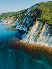 Aerial view of scenic coastline with sea and rocky cliffs with pine forest. Summer day on sea