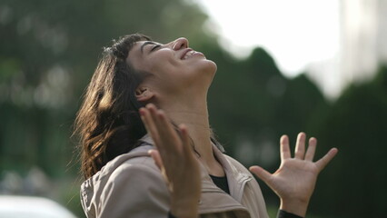 Evangelical South American woman standing outside feeling the presence of God arms in the air looking at sky with FAITH