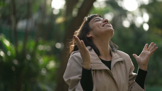Evangelical South American woman standing outside feeling the presence of God arms in the air looking at sky with FAITH