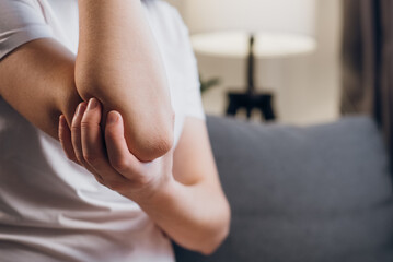 Health, arthritis of joints pain in elbow concept. Close up of unrecognizable unhealthy young caucasian woman with elbow pain, doing massage sitting on grey couch at home