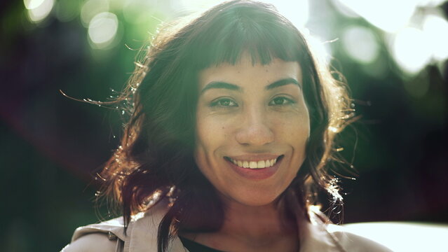 A young Brazilian woman smiling at camera sun flare. South American confident person standing outside