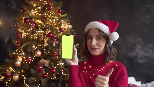 Woman in red sweater and Santa's hat holding a mobile phone with a green screen