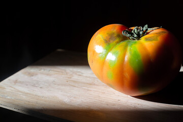 Big red and green tomato with in contrast Rembrandt sunlight. One isolated vegetable on wooden...