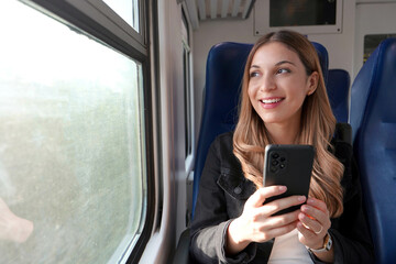 Portrait of young satisfied woman traveling with public transport holding mobile phone sitting and...