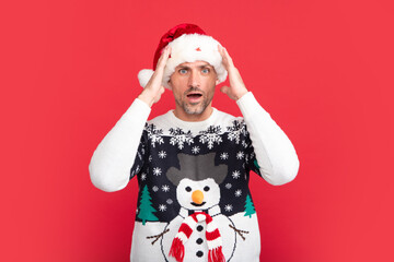 Studio portrait of guy wears santa hat and winter sweater. Man with christmas hat over isolated red background.