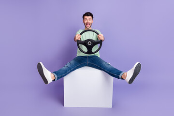 Full size photo of handsome man sit white cube hold steering wheel crazy dressed stylish gray look isolated on purple color background