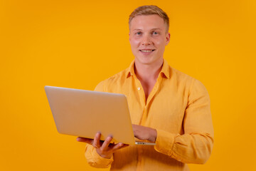 Caucasian blond businessman man on a yellow background, portrait with a laptop smiling