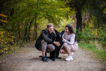 Young lovely couple husband and wife embracing huging their dog Black Labrador retriever on a woods street blur. Concept: veterinary medicine, animal care and care, dogs, pets, lifestyle. a family