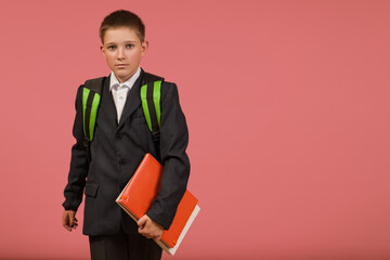 schoolboy in a black suit with a briefcase and a book on a colored background with copy space