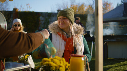 Adult woman chooses apples at the stall with fruits and vegetables. People walking and shopping on...
