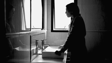 Suffering woman in front of bathroom mirror in mental disorder feeling anxiety in monochromatic