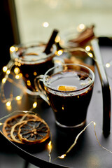 Christmas mulled red wine with spices and oranges on a black table with light garland, traditional hot drink at Christmas, festive cocktail