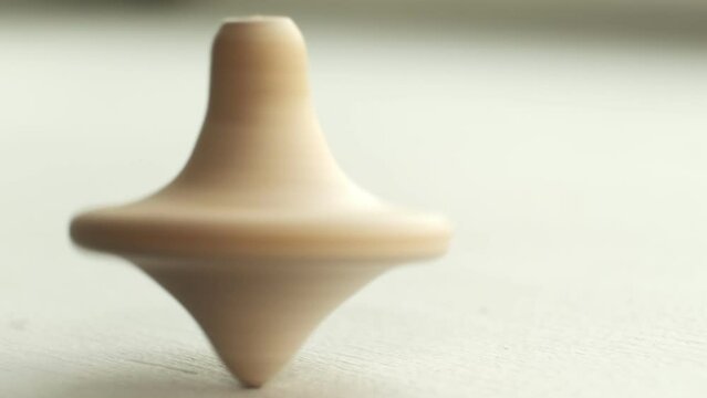 wooden toy spinning top is spinning on a white table. The top slows down, losing balance or stability and falls on its side. The end of the movement