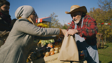 People shopping, choosing fruits and vegetables at local farmers market, packing goods in eco bags. Autumn fair on weekend outdoors. Vegetarian and organic food. Agriculture. Points of sale system.