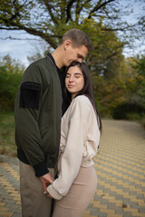 Fototapeta premium Young man and woman cuddle outside in an autumn or spring park. Autumn park is on background,love concept,happy lifestyle. Stylish adults wear warm clothes