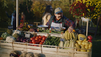 Farmer with bushy mustache lays out fruits and vegetables. Owner of point of sale looks forward to...