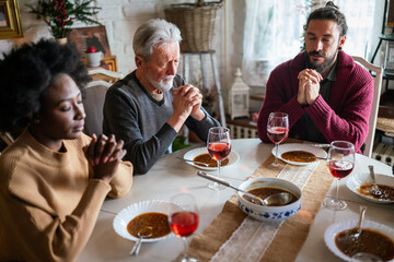 Family and religious concept. Group of multiethnic people with food praying before meal