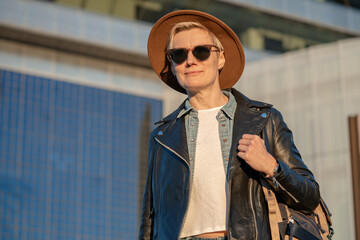 30s woman with short blonde hair in leather jacket and trendy hat walking in city with modern building in Barcelona