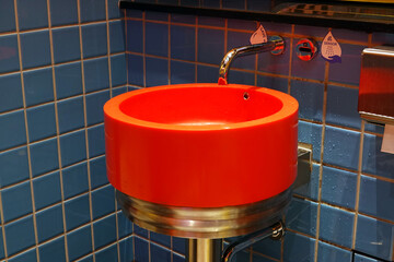 Bathroom sink basin orange color and faucet. Blue color tiled wall background. Round wash basin, modern toilet design.    