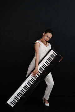 the girl effectively poses with a synthesizer and smiles on a black background