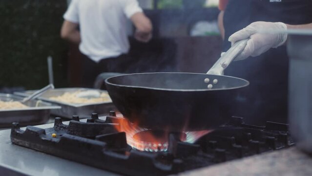 Chef working in restaurant kitchen - preparing a delicious traditional asian meal, tossing the food in the air turning it in the pan. Chef preparing flambe dish.